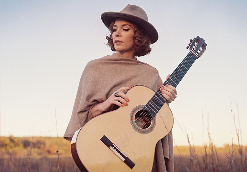 Sue Foley holding a guitar in a field.